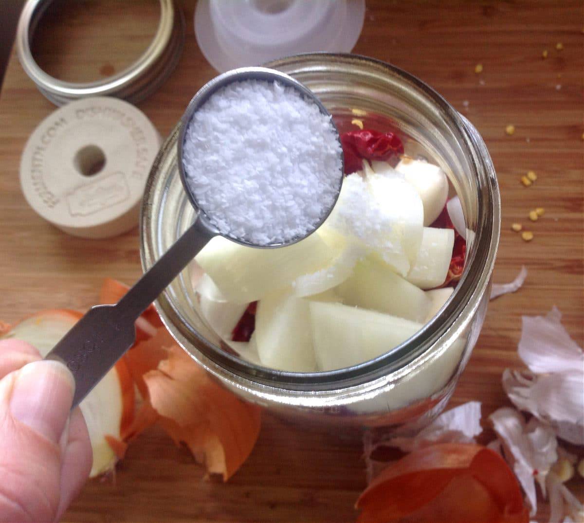 a hand adding salt to the jar of peppers and onions