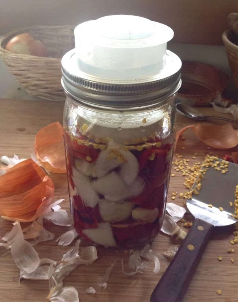 peppers and onions in a jar with an airlock ready to ferment into hot sauce