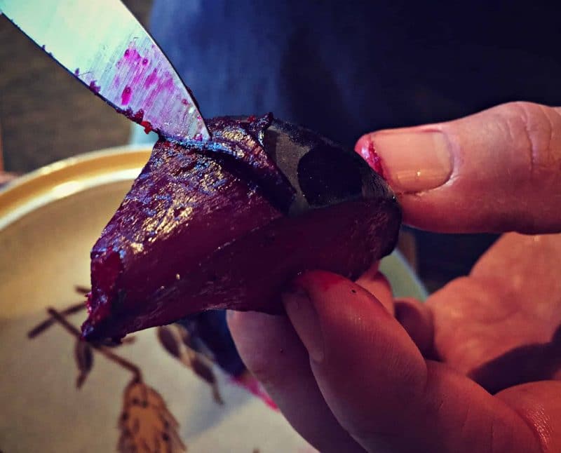 a hand peeling beets with a small knife