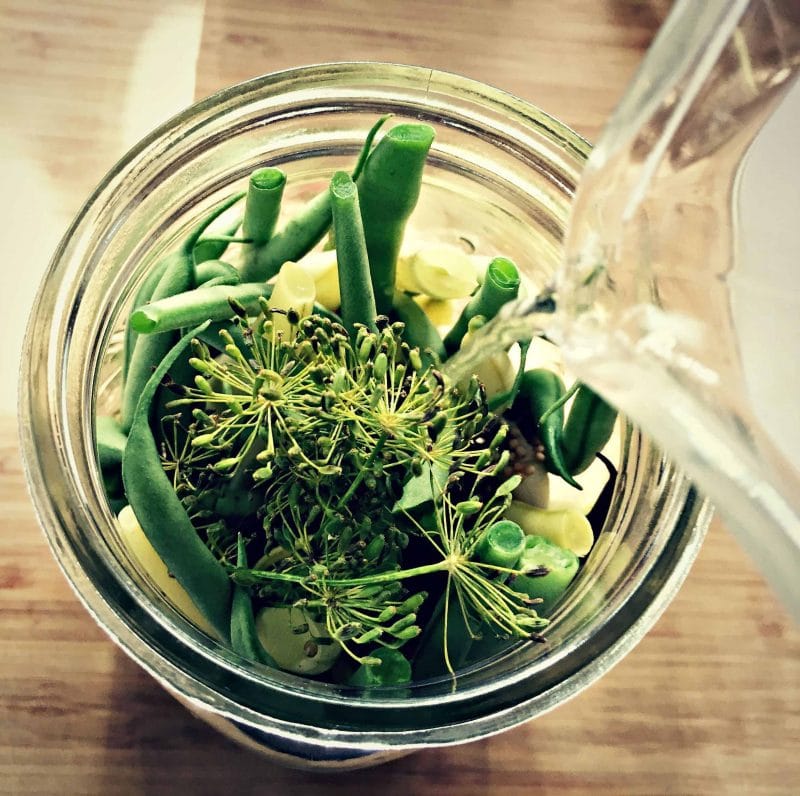 pouring brine over beans in jar