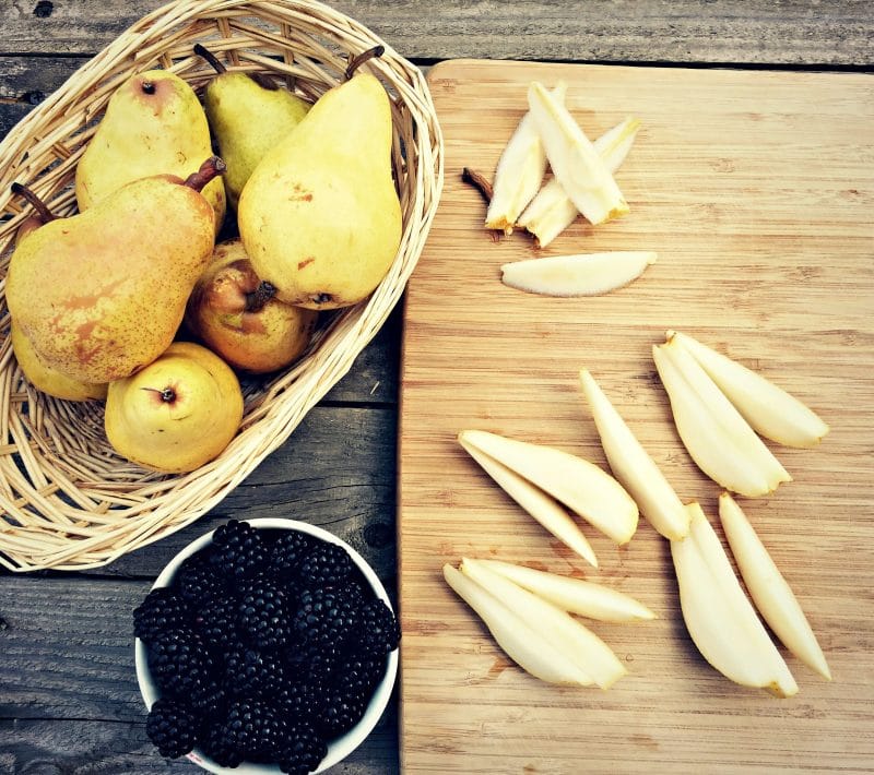 sliced pears on cutting board next to basket of pears and bowl of blackberries