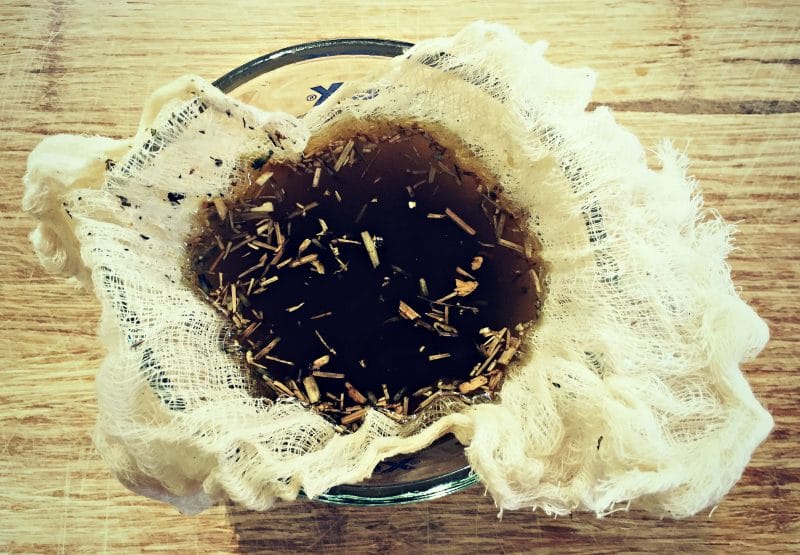 straining out herbs from the salve mixture using a cheesecloth