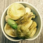 Fermented green tomatoes in a white dish on a wood surface, top view.