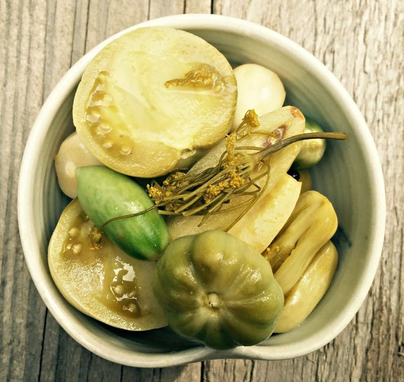 Fermented green tomatoes in a white dish on a wood surface, top view.