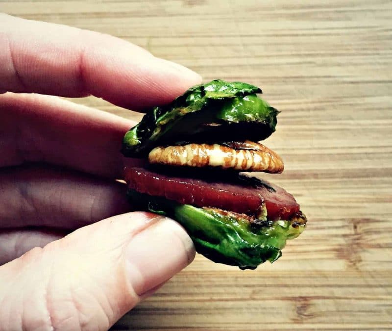 a hand holding a brussles sprout, pecan, and bacon sandwich