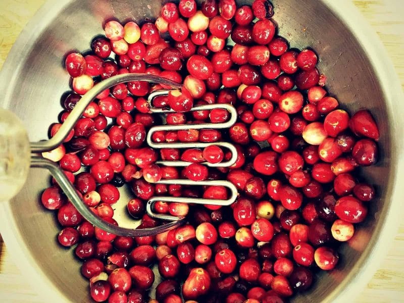 a potato masher smashing cranberries