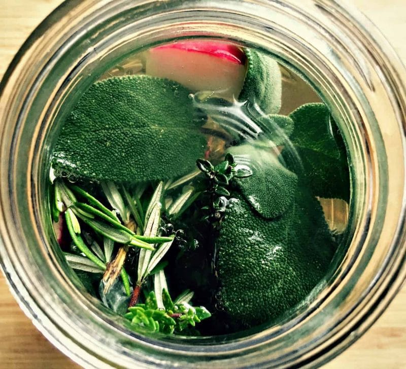 A jar of kvass fermenting with fresh herbs and a radish, top view. 