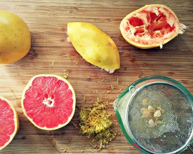 straining the grapefruit juice with halved red grapefruits on a wooden board