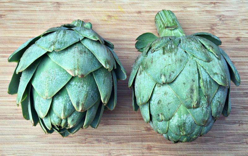 two fresh artichokes on a cutting board