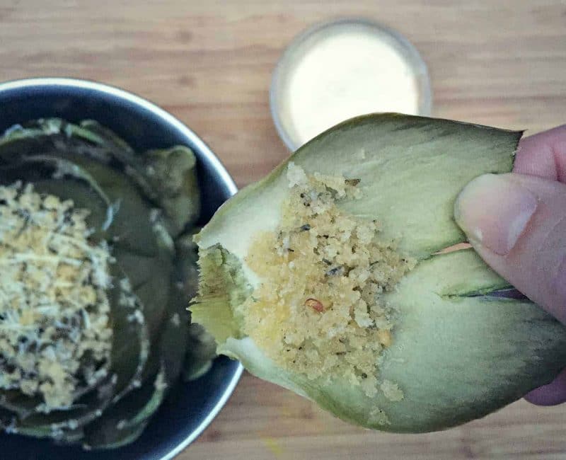 a hand holding a stuffed artichoke leaf