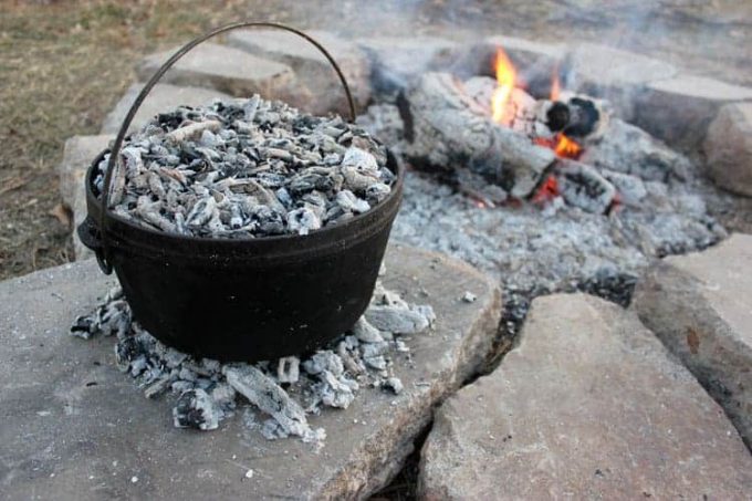 Dutch oven on hot coals by a fire