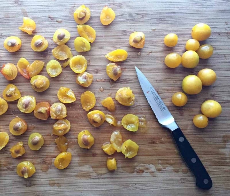 pitting small yellow plums on a cutting board