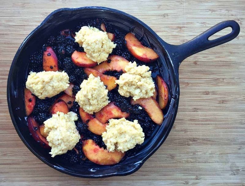 blackberries and peaches in a cast iron skillet with cobbler biscuit dough on top