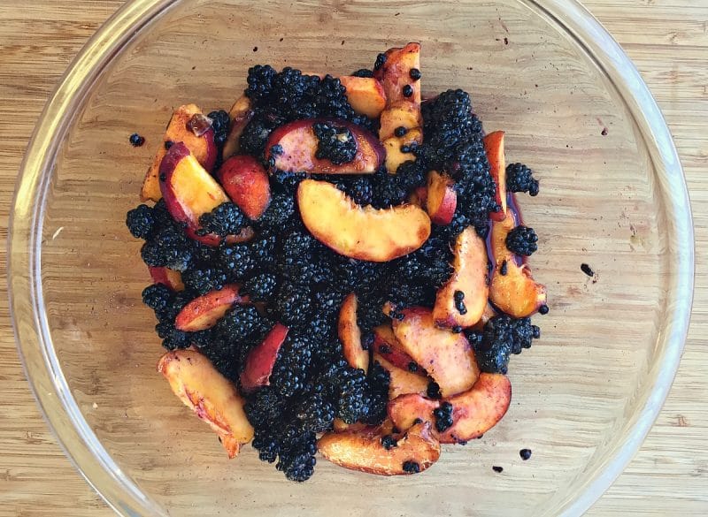 glass bowl with peach and blackberries on wood counter