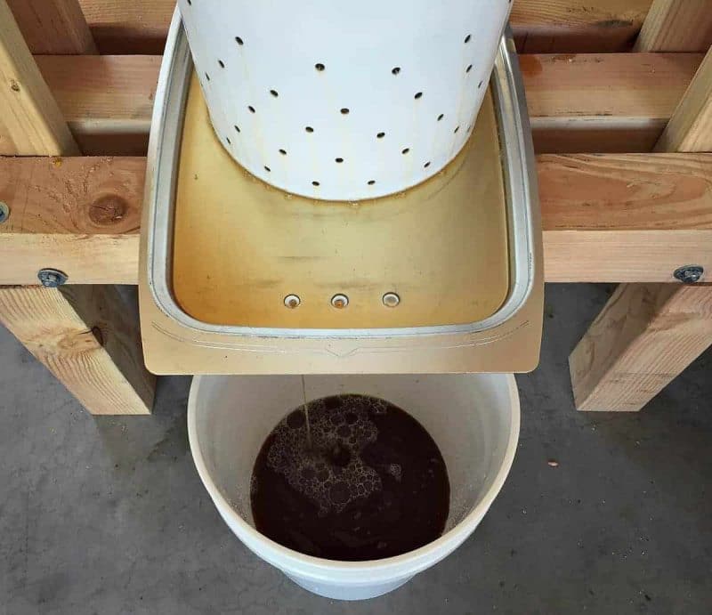 apple juice flowing through the holes of the homemade cider press