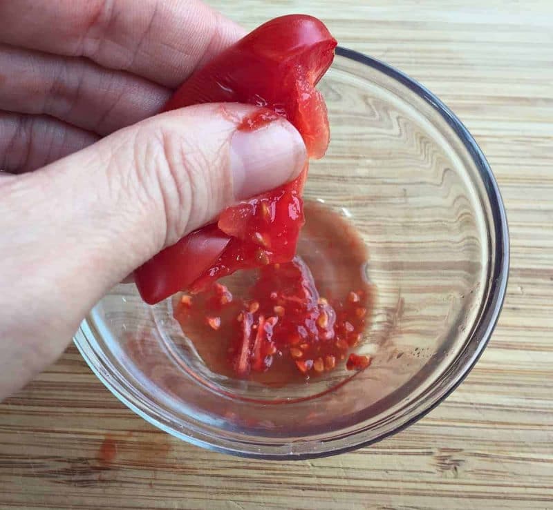 squeezing out tomato seeds into a bowl