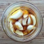 An overhead view of fermented honey garlic in a glass jar on a wood background.