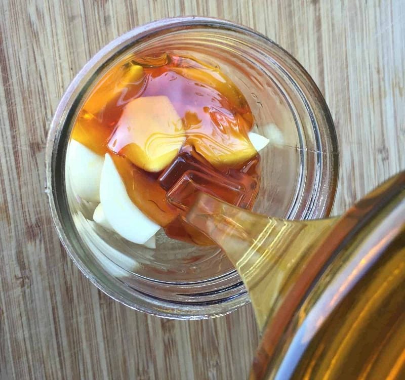pouring honey over garlic cloves in a jar