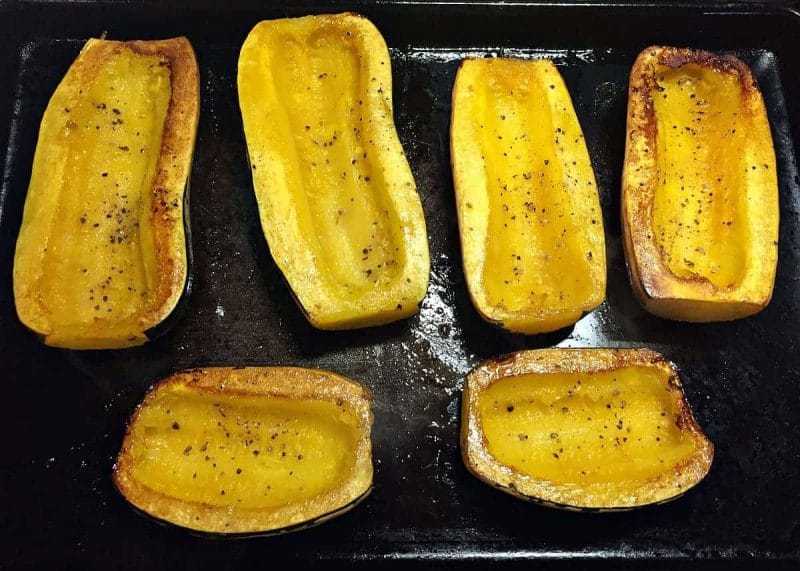 Roasted delicata squash halves on a baking sheet.