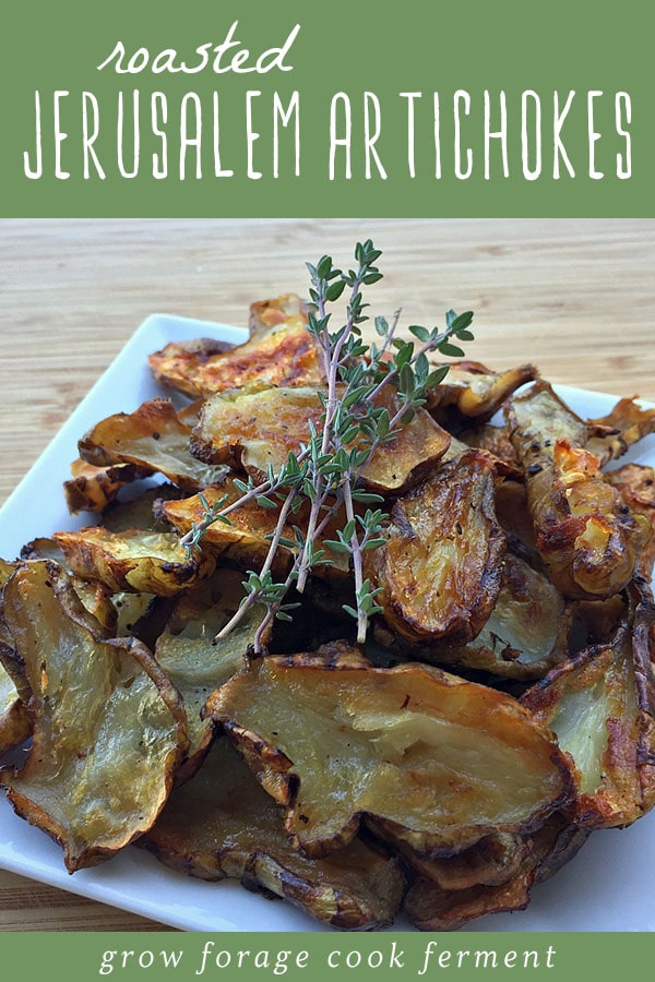 Sliced and roasted Jerusalem artichokes on a white platter garnished with fresh thyme.