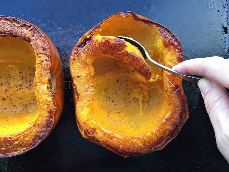 Scooping out roasted pumpkin with a spoon.