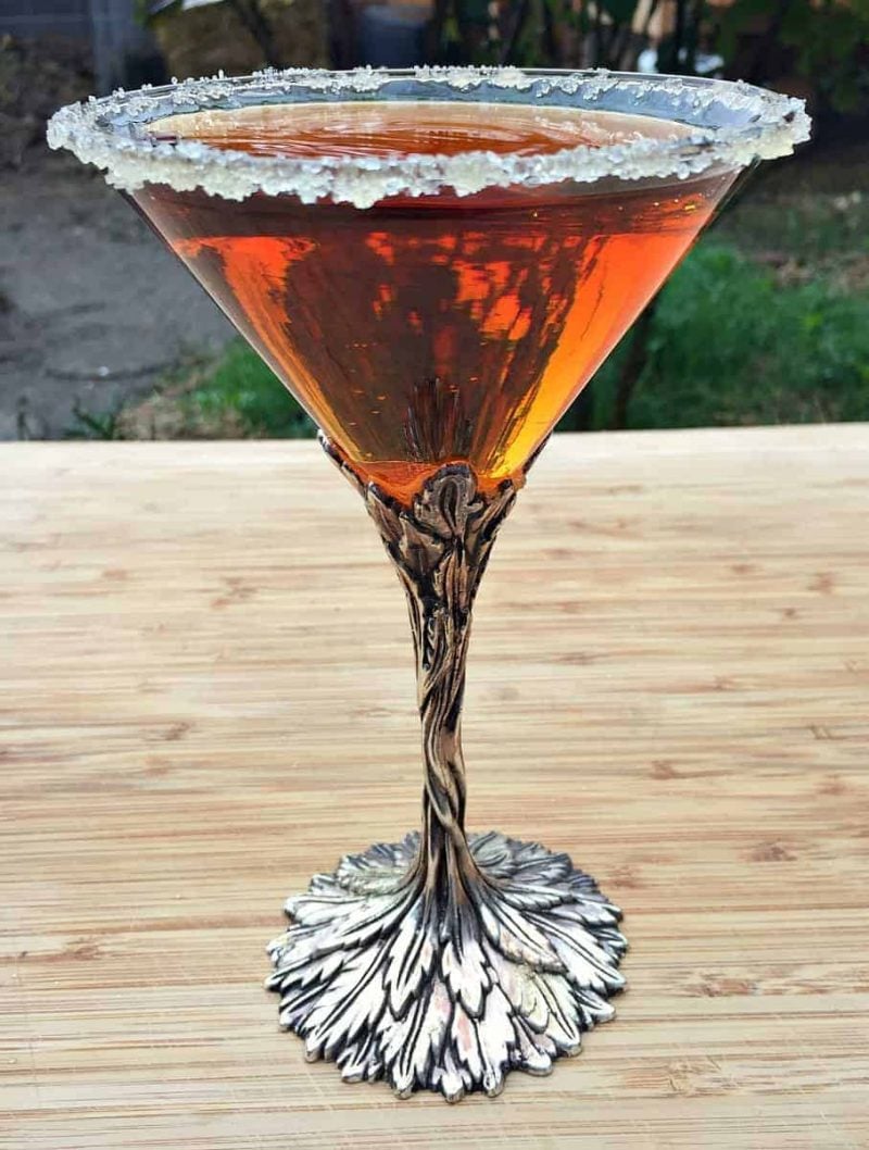 Conifer infused vodka in a martini glass with a silver stem in the shape of leaves. 