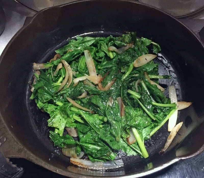 a cast iron skillet with sauteed turnip greens and onions