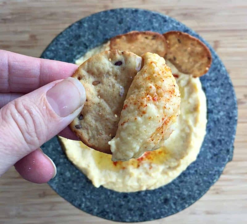 a hand holding a cracker with homemade hummus
