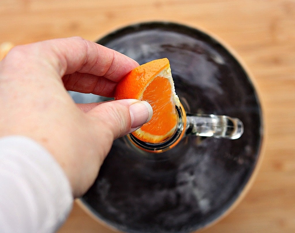 a hand putting an orange slice into the jug of maple mead
