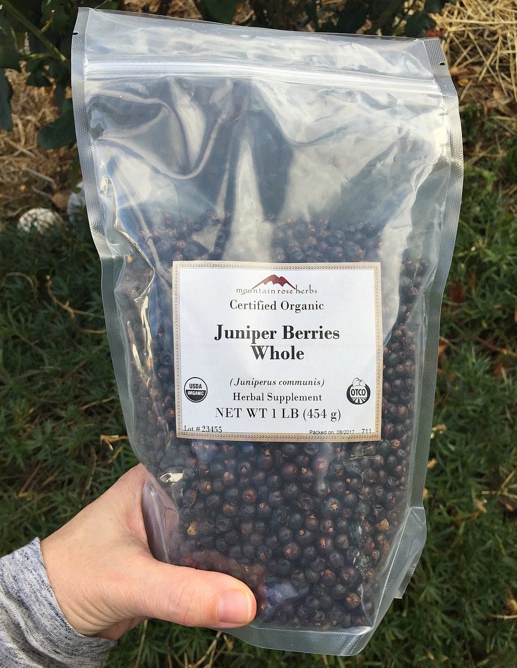 a hand holding a bag of dried juniper berries from mountain rose herbs
