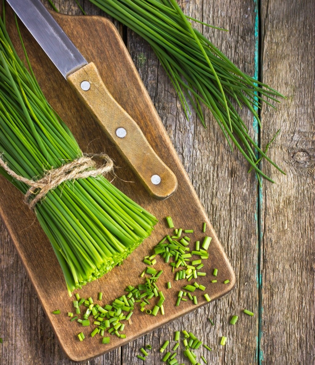 bunch of fresh chives on a wooden cutting board, top view