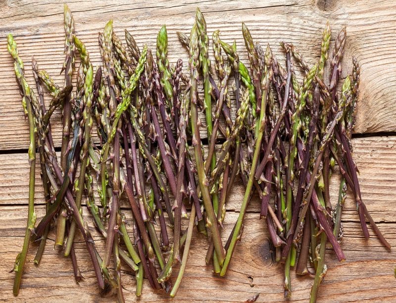 a bunch of purple and green asparagus on a wooden surface