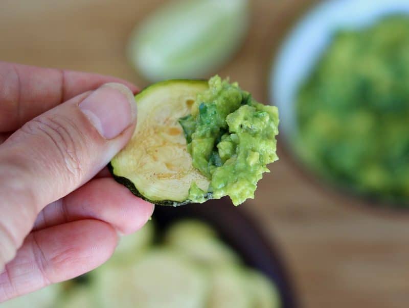 a hand holding a zucchini chip with guacamole