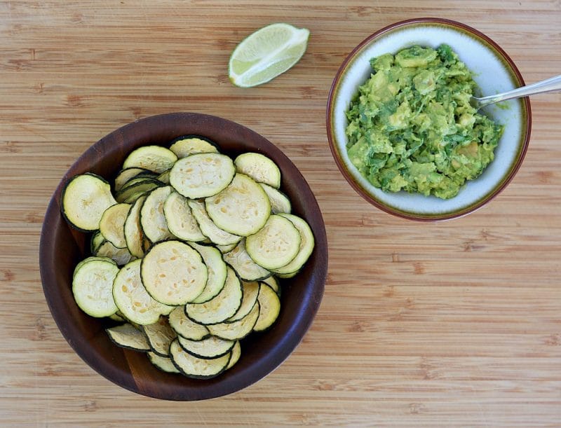a wooden bowl of zucchini chips and a small bowl of guacamole