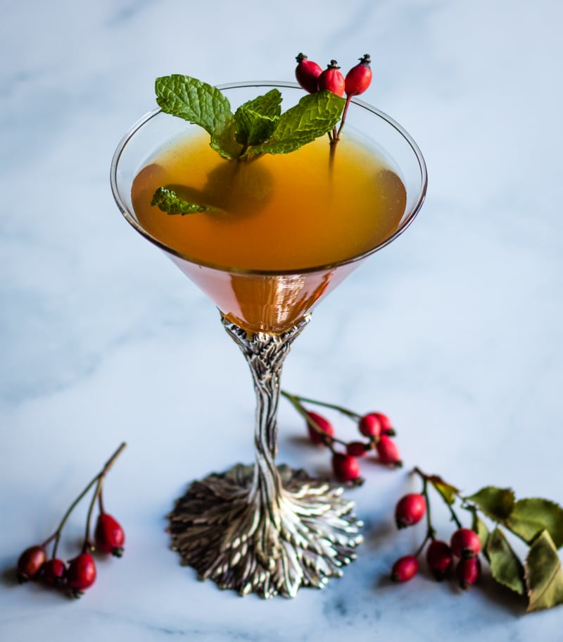 rose hip whiskey smash in a martini glass garnished with fresh mint and rose hips