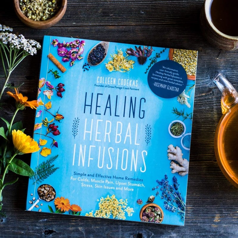 the book Healing Herbal Infusions on a wooden board with flowers and tea