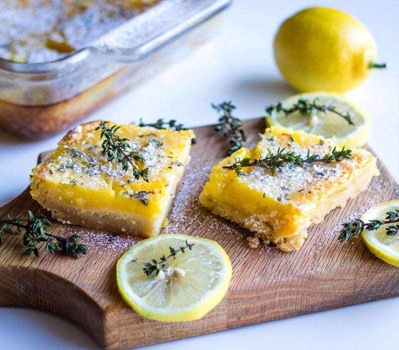 two lemon bars with thyme on a wooden serving board