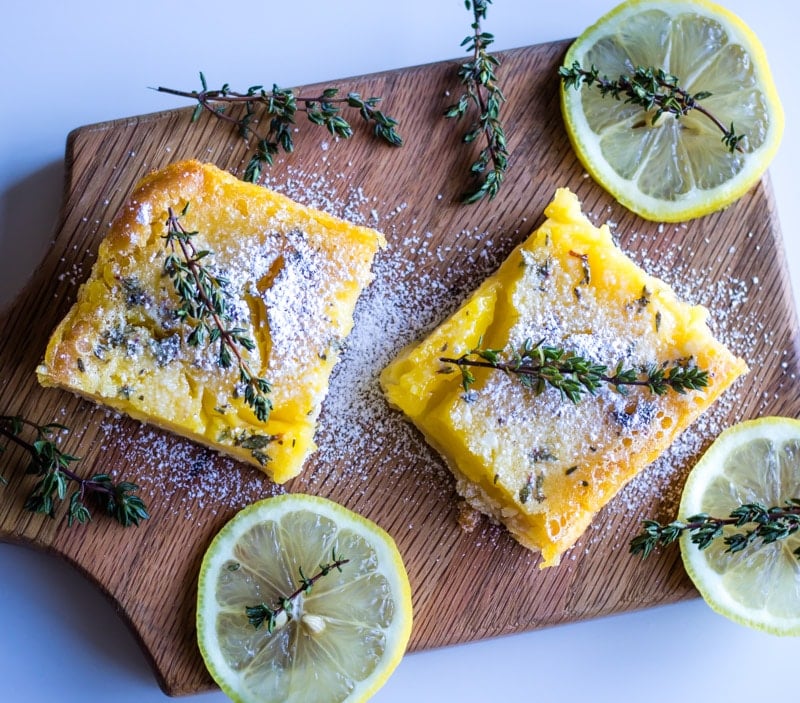 lemon bars on wooden cutting board with lemon slices and fresh time