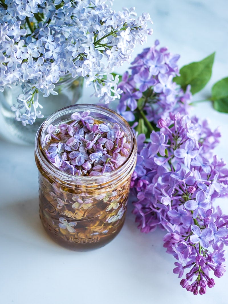 a jar of lilac flower honey with with and purple lilac blossoms