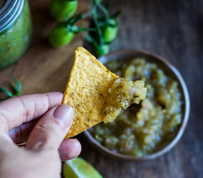 a hand holding a chip with green salsa
