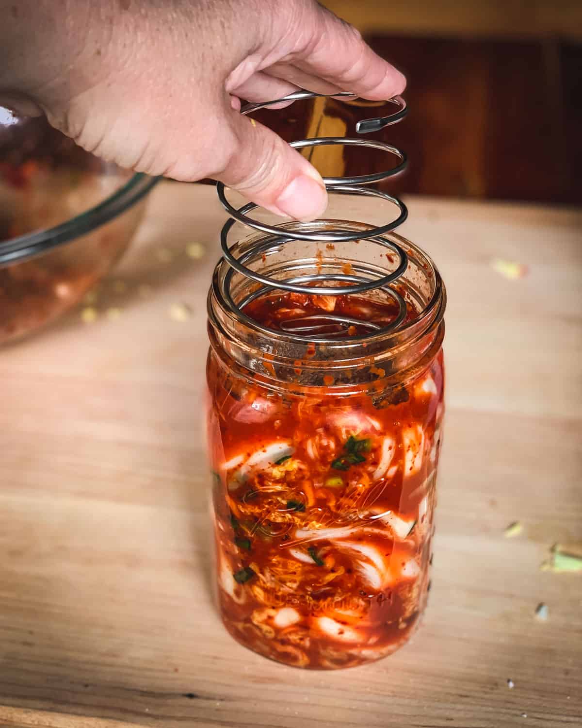 putting the fermenting spring into the jar of kimchi