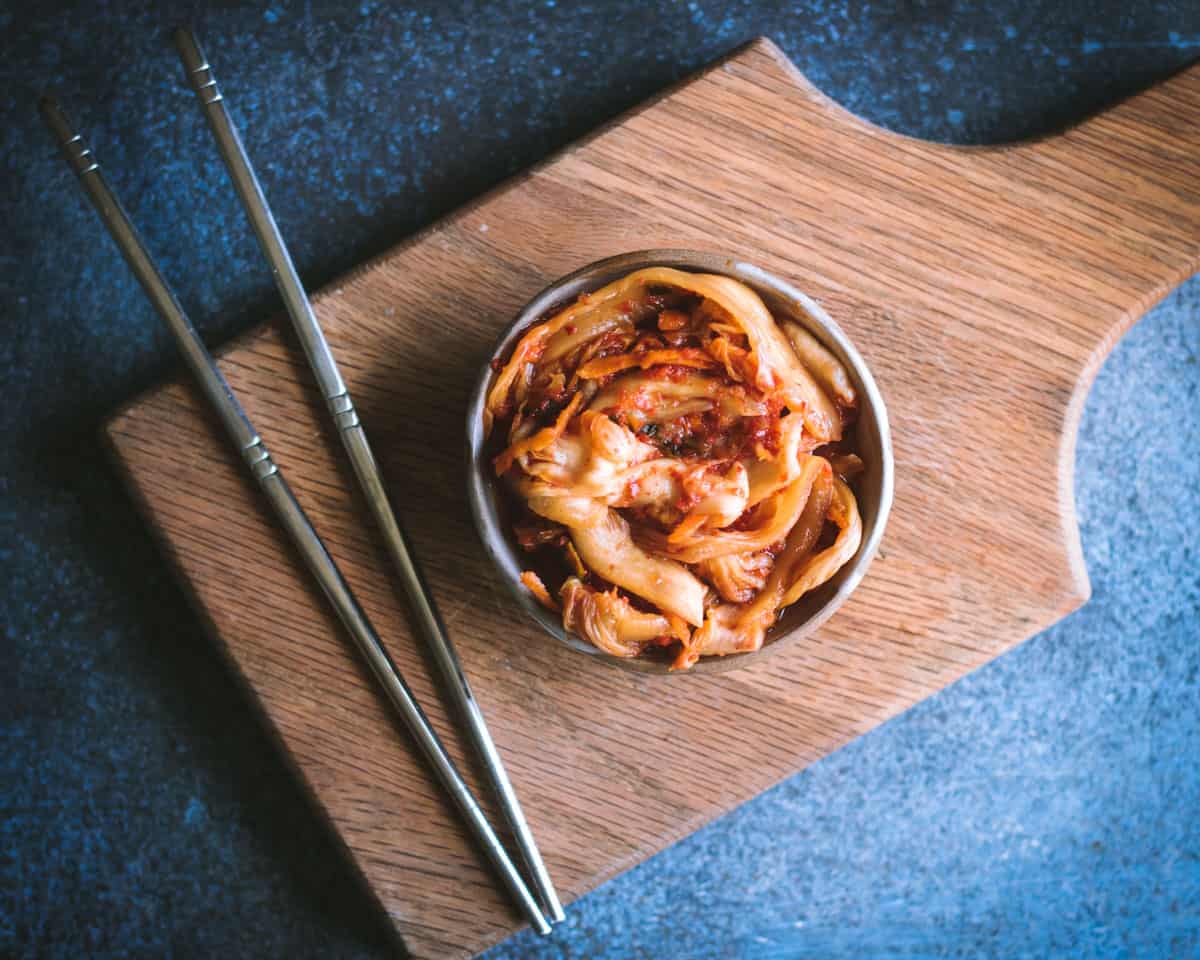 a small bowl of kimchi on a cutting board with chopsticks