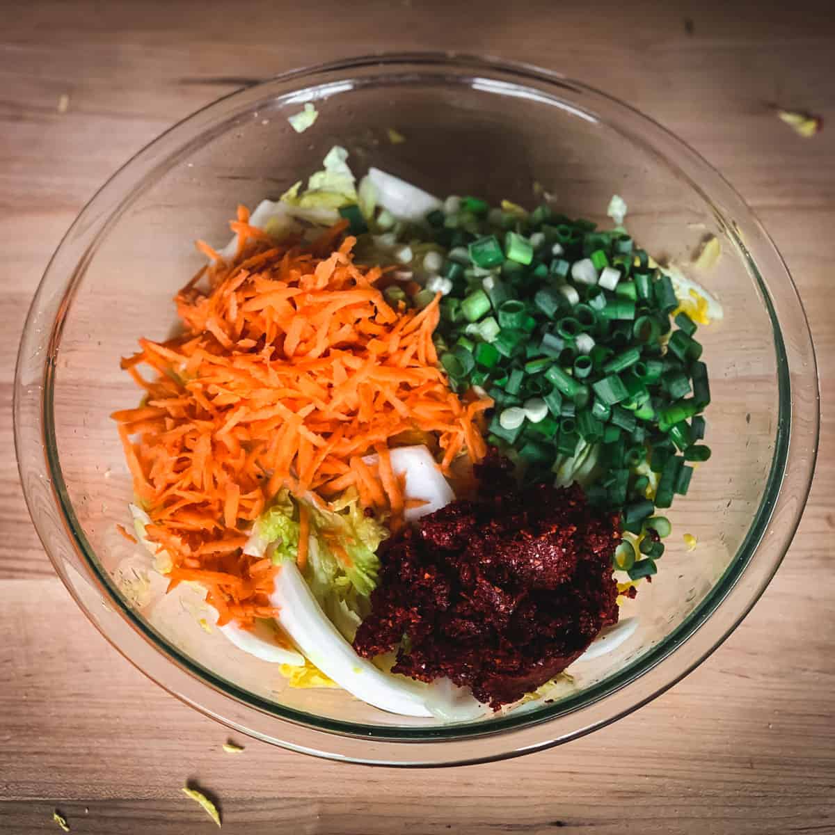 adding the carrots, onions, and spices to the bowl of cabbage