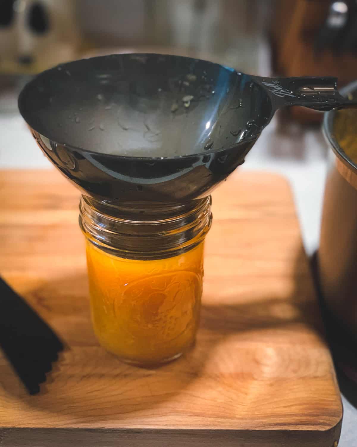using a canning funnel to fill the jar with peach jam