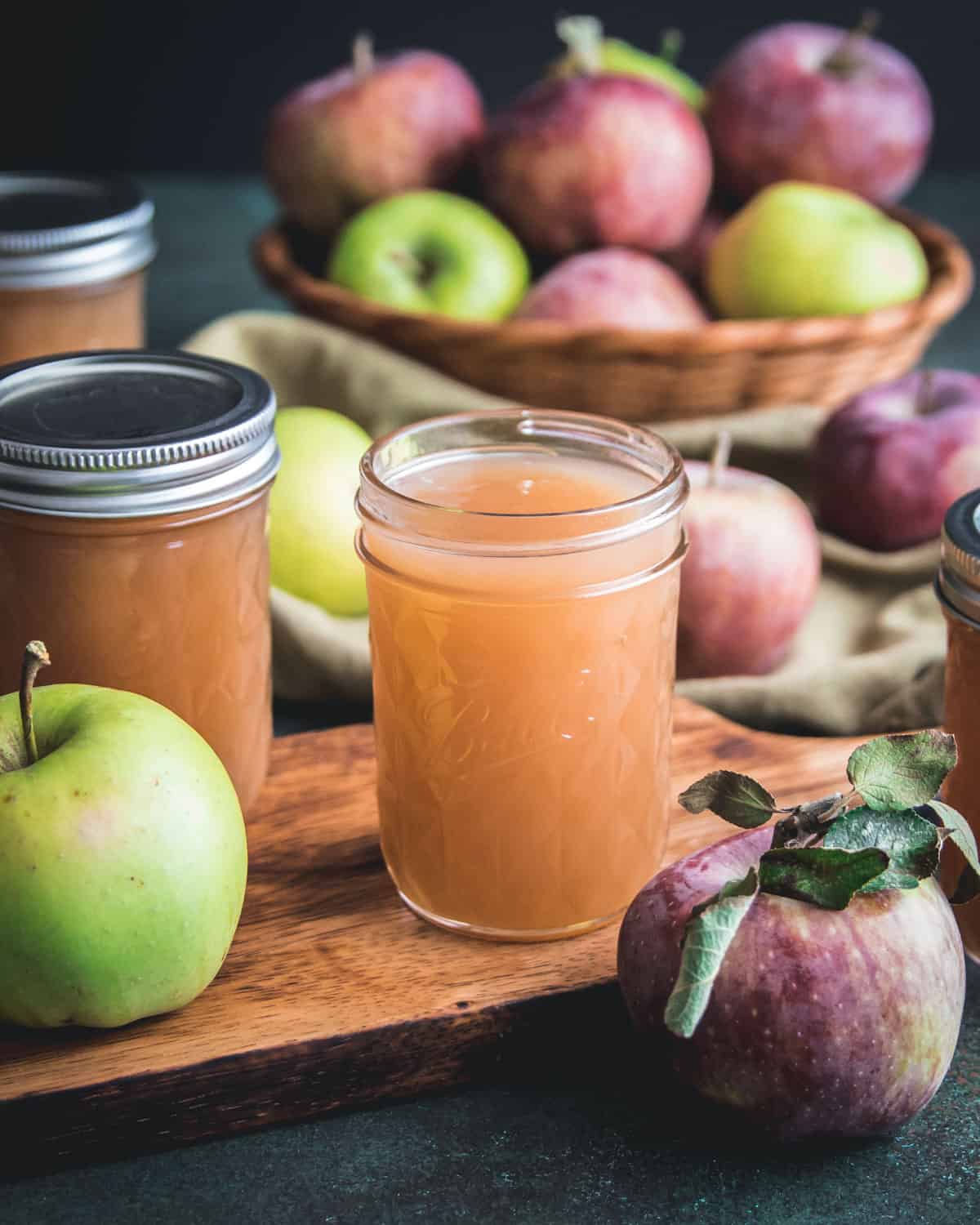 an open jar of apple jelly on a cutting board with apples