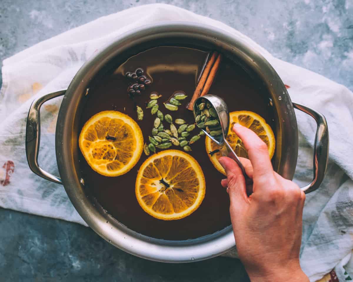 a hand adding mulling spices to the pot of hard cider
