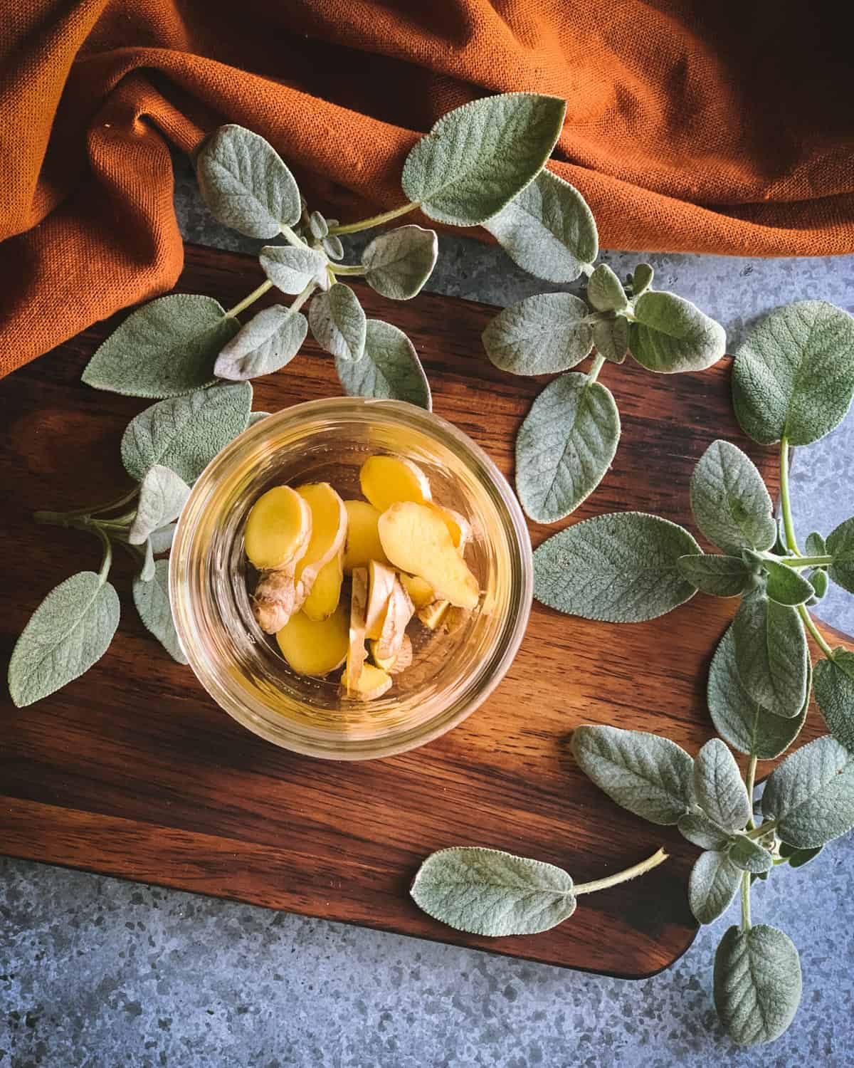 sliced ginger pieces in a pint jar with sage on the table