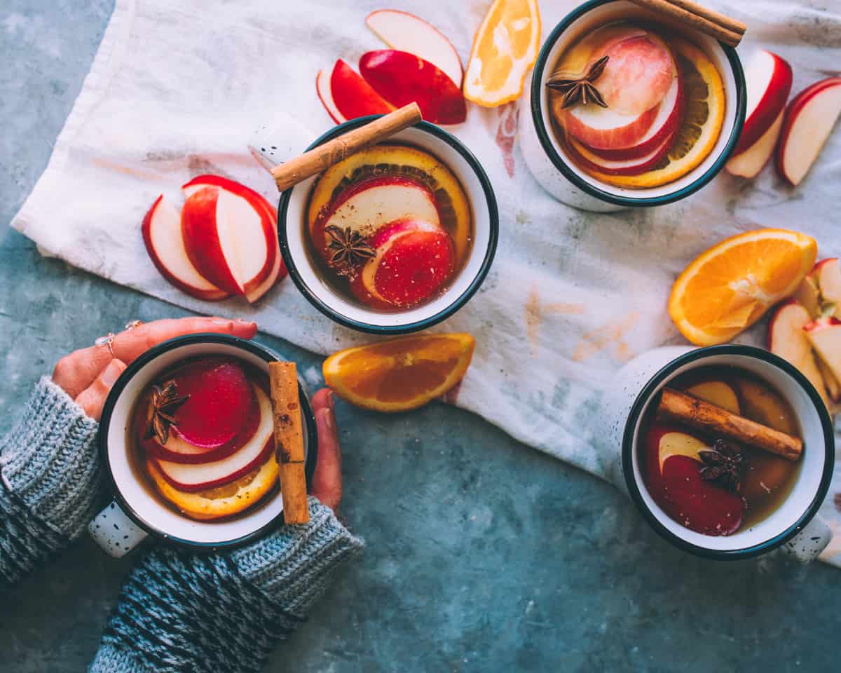 four mugs of mulled hard cider with two hands wrapped around one of them