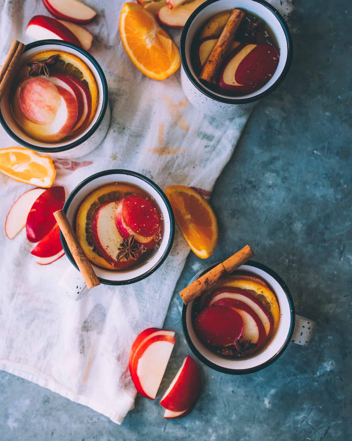 four mugs of mulled hard cider on a table with garnishes