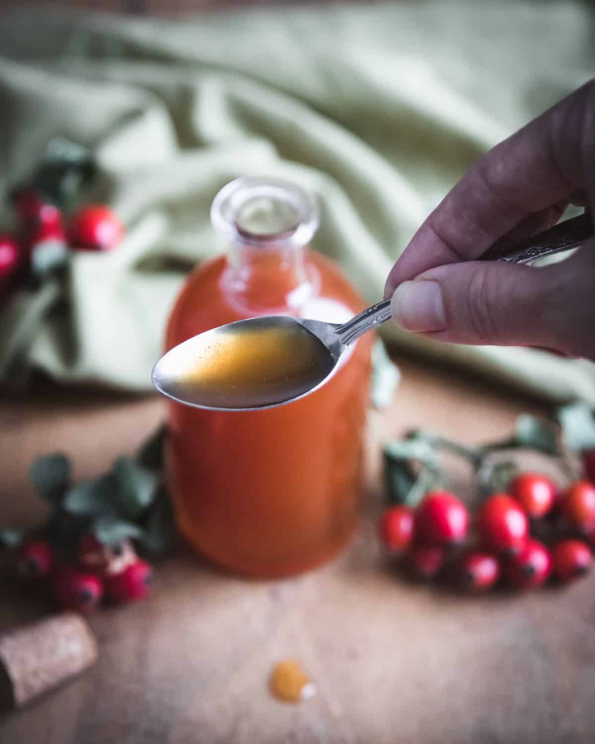 a hand holding a spoonful of rose hip syrup